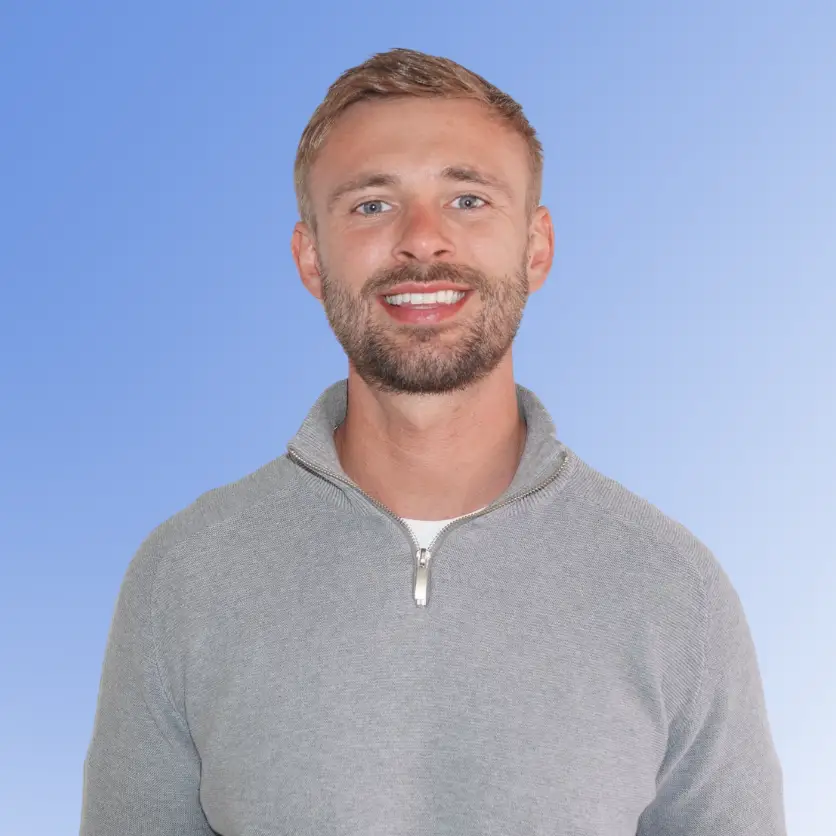 Connor Burns, Recruitment Consultant at ACE Partners, smiling in a light grey quarter-zip sweater against a blue background.