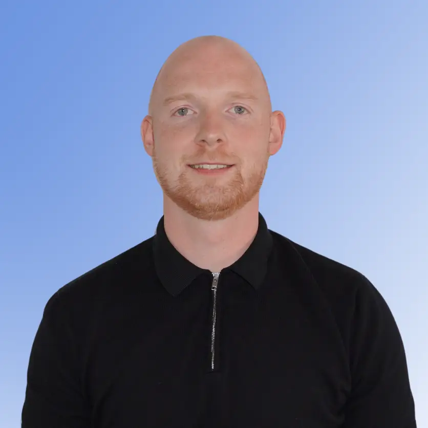 Dan Ovenden, Head of Contract at ACE Partners, smiling in a black zip-collar shirt against a light blue background.