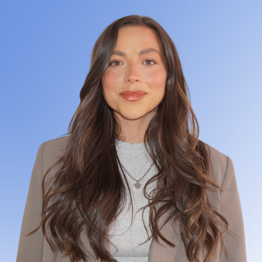 Tia Smith, Recruitment Consultant at ACE Partners, wearing a grey top and blazer with long wavy hair against a blue background.